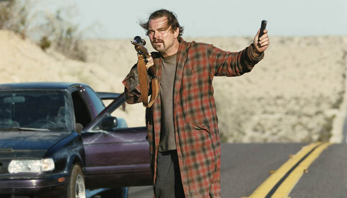 Mann steht mit einer Waffe vor einem Auto