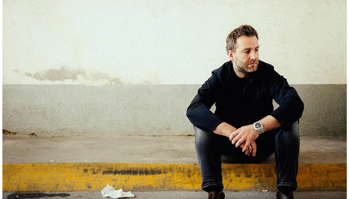 Mann sitzt vor weißer Wand