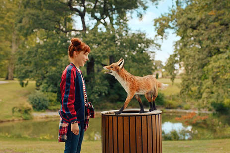 Mädchen spricht mit einem Fuchs vor einem See in einem Park
