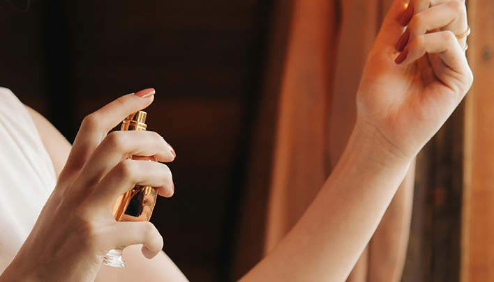 Frau sprüht sich Parfüm auf die Haut