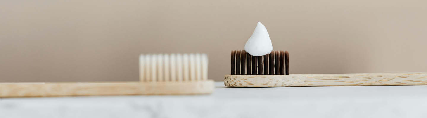 Zwei Holzzahnbürsten, auf einer davon ist ein Klecks mit Zahnpasta