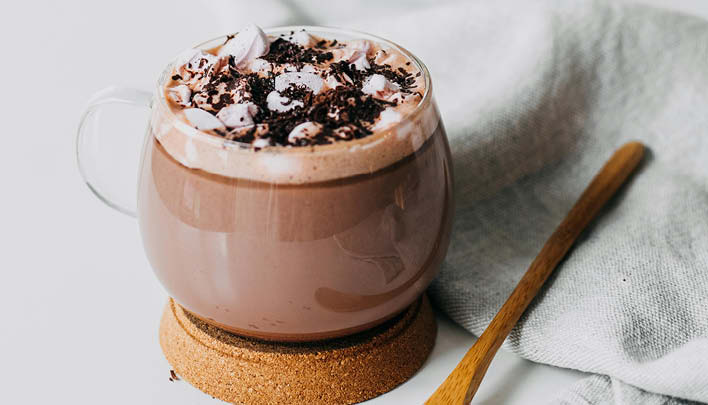 Heisse Schokolade im Teeglas Holzloeffel weisser Hintergrund