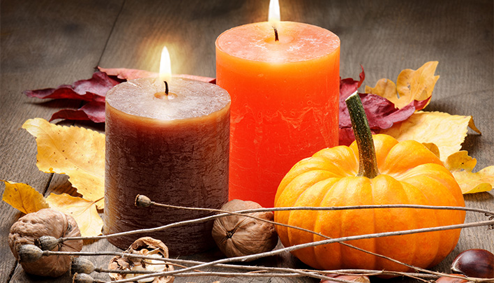 Zwei Kerzen in Orange und Dunkellila neben einem Kürbis.