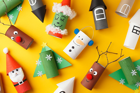 Verschiedene weihnachtliche Figuren aus leeren Toilettenrollen auf gelbem Hintergrund