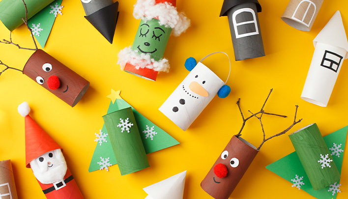 Verschiedene weihnachtliche Figuren aus leeren Toilettenrollen auf gelbem Hintergrund