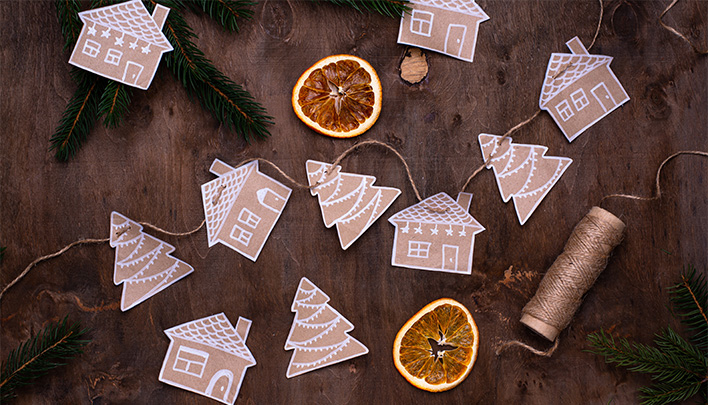 Weihnachtliche Girlande mit Tannenbäumen und Häusern aus hellbraunem Tonpapier auf dunkelbraunem Hintergrund