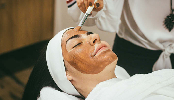 Kosmetikerin trägt Gesichtsmaske auf