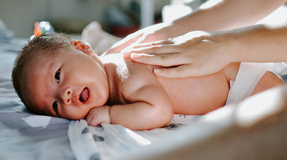 baby-liegend-sonnenlicht-frauenhaende-auf-ruecken-575x320-85338-0