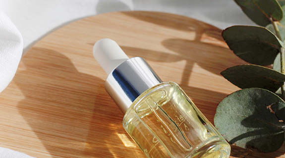 lifestyle-pipttenflaeschchen-oelige-fluessigkeit-liegend-auf-holzbrett-eukalyptuszweig-seitlich-575x320-90658-0