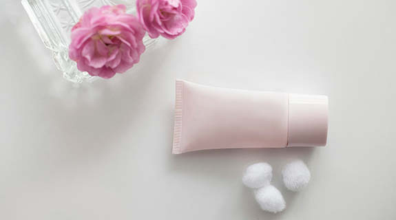 lifestyle-flatlay-mit-rosa-tube-drei-weisse-wattebaeuschchen-zwei-rosa-blumen-weisser-hintergrund-575x320-91992-0