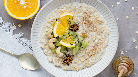 lifestyle-weisser-teller-mit-porridge-cashews-kiwi-nelken-zimt-orange-honigloeffel-silberloeffel-weisses-tuch-575x320-90552-0