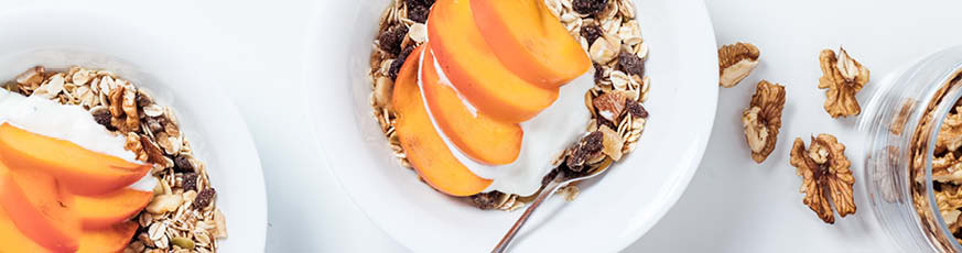 lifestyle-zwei-weisse-schalen-mit-muesli-joghurt-kaki-walnuessen-weisser-hintergrund-873x230-90547-0