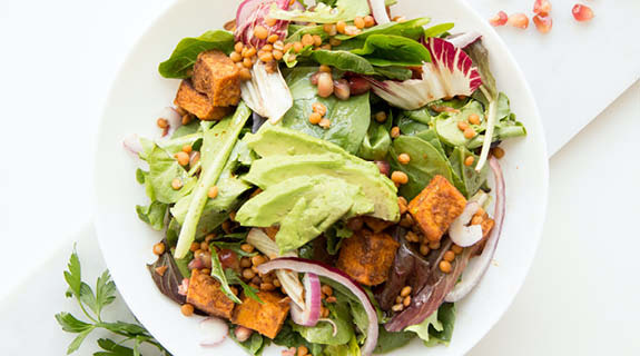 lifestyle-weisser-teller-mit-gruenem-salat-avocado-tofuwuerfel-zwiebelringe-radicchio-samen-granatapfelkerne-weisser-hintergrund-575x320-92068-0