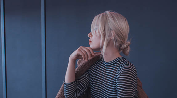 lifestyle-frau-profilansicht-blonder-dutt-gestreifte-oberteil-dunkler-hintergrund-575x320-98691-0