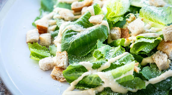 lifestyle-weisser-teller-mit-caesarsalad-gruener-salat-croutons-parmesan-helles-dressing-575x320-92064-0