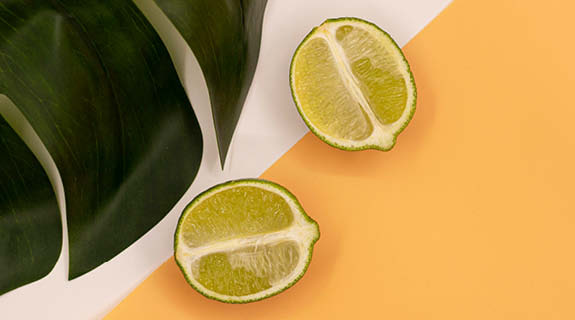 lifestyle-zwei-halbe-limetten-orange-weisser-hintergrund-gruenes-blatt-04-24-96439-0