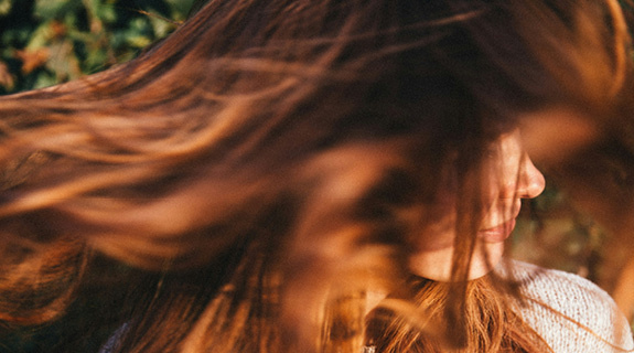 lifestyle-rothaarige-frau-lange-haare-grauer-pulli-gru-ene-bla-etter-im-hintergrund-575x320-98519-0