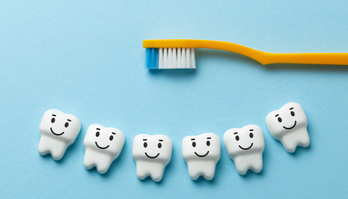 Modell-Zähne mit lachenden Gesichtern auf blauem Hintergrund, dazu eine Zahnbürste