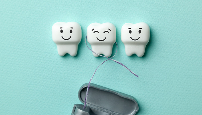 Modell-Zähne mit lachenden Gesichtern auf türkisem Hintergrund und Zahnseide