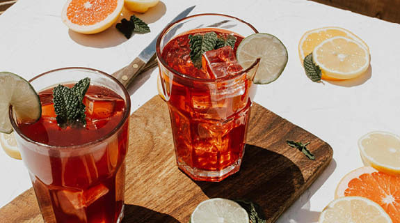 lifestyle-weisse-tischplatte-orangenscheiben-zitronenscheiben-holzbrett-messer-zwei-drinks-eiswuerfel-minze-04-24-96538-0