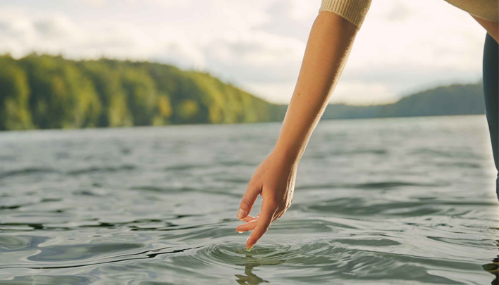 Hand berührt die Oberfläche eines ruhigen Sees in natürlicher Umgebung