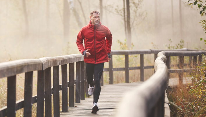Person joggt auf einem Holzsteg durch nebeligen Wald
