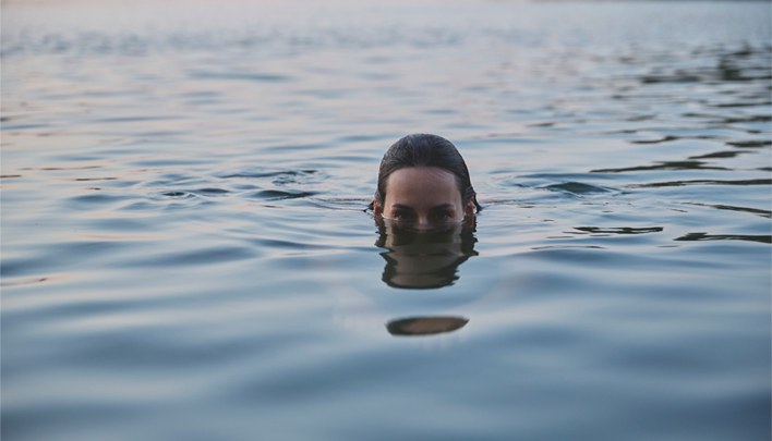 Person schwimmt im ruhigen See bei Sonnenuntergang