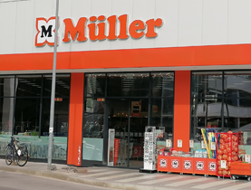 Exteriér modernej predajne Müller s oranžovým logom a vstupnou zónou.