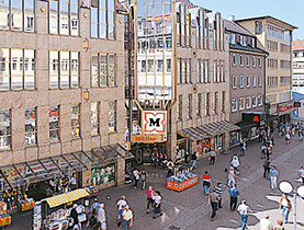 Predajňa Müller z 90. rokov v rušnej pešej zóne s logom nad vchodom.