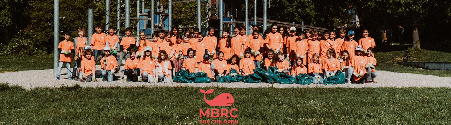 Skupina detí v oranžových tričkách s nazbieranými vrecami odpadu na ihrisku počas akcie MBRC the children.